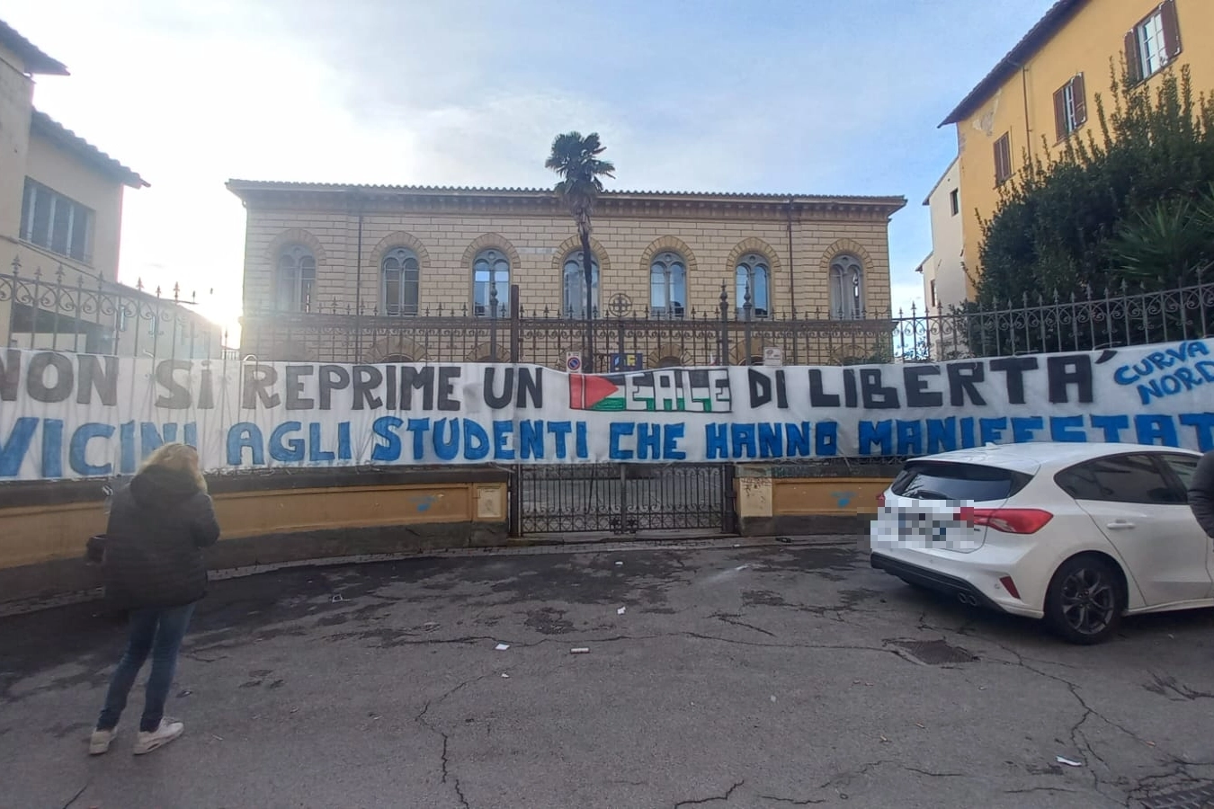 Lo striscione degli ultras del Pisa attaccato alla cancellata della scuola Russoli, dove ieri gli studenti sono stati picchiati con i manganelli