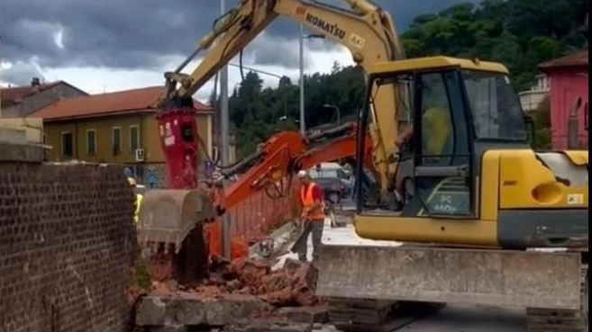 La ruspa al lavoro per abbattere il vecchio muro lungo la linea ferroviaria dismessa