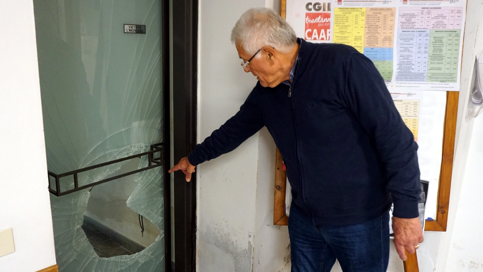 Un uomo mostra con la mano la porta danneggiata da chi la notte tra giovedì e venerdì è entrato nella sede della Cgil alla ricerca di oggetti da rubare