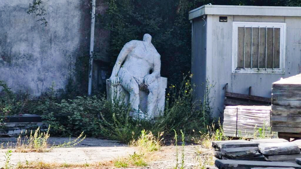 La statua dell’Uomo seduto è stata “parcheggiata” all’interno di un magazzino del Comune tra container, attrezzi e erba alta