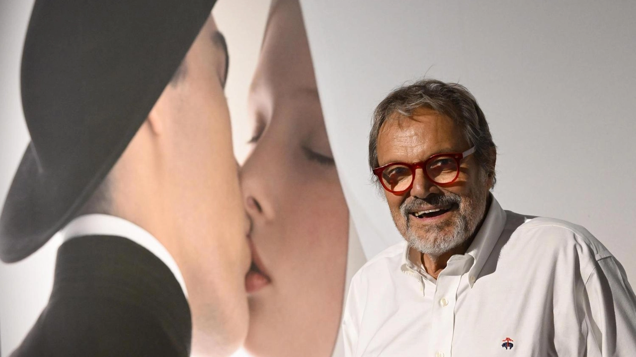 Oliviero Toscani accanto a uno dei suoi scatti più celebri realizzati per la Benetton e destinati a far parlare di sé per il contenuto ’trasgressivo’