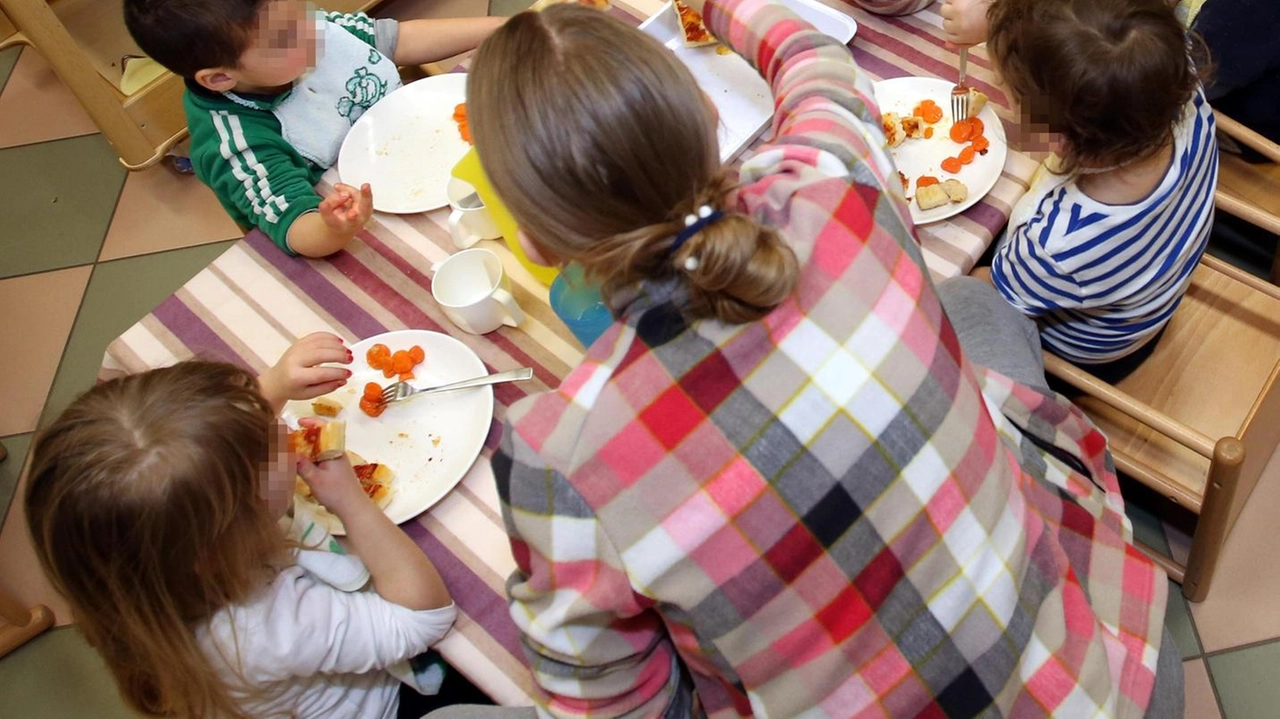 Bambini di un asilo nido durante l’orario della mensa insieme al personale scolastico in una foto di repertorio